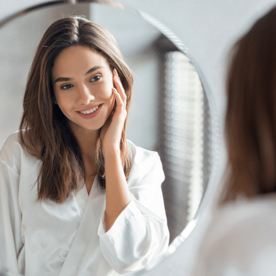 Woman examining her skin in a mirror, representing skincare myths vs. Evidence-based skincare practices for achieving healthier, well-balanced skin.